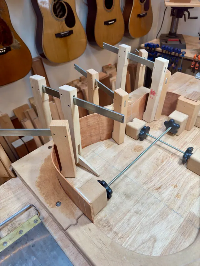 A rim clamped in the workboard, vintage guitars hanging on the wall behind