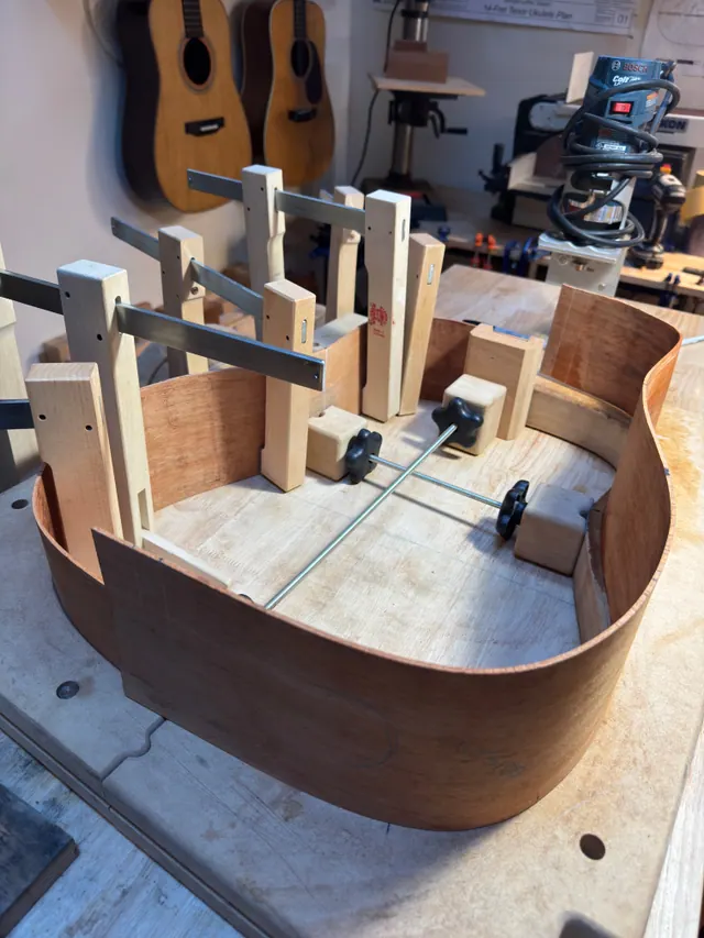 A rim clamped up in the workboard under the wall of vintage guitars