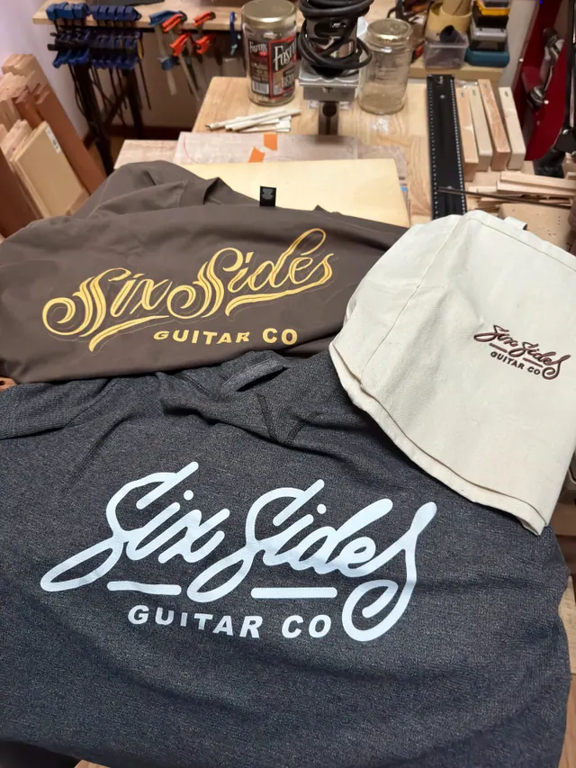 Six Sides Guitar Co. shirts and a canvas tote laid out on the bench