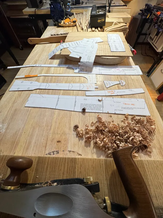 Paper templates and a hand plane laid across the bench with a pile of shavings
